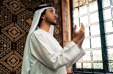 Man from emirati wearing kandura outfit spending time in an arabian traditional house in Dubai. Young man praying in the mosque.