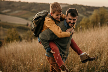 Cheerful dad carrying his teenage son on his back in nature on a beautiful day