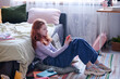 © AnnaStills - Side view shot of teen girl with red hair sitting on floor in her bedroom looking at smartphone screen, copy space