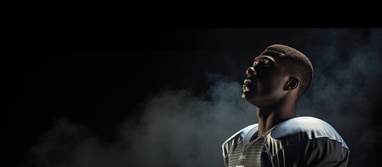 An American football player gazing downward with a spotlight illuminating the sky in the background Copy space image