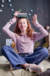 © AnnaStills - Vertical medium shot of teen girl sitting on bed posing for camera with books on head