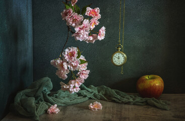 Wall Mural - Still life with a branch with pink sakura flowers, a pocket watch on a chain and a ripe apple on a dark background.