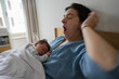 © Marco - A mother yawns while holding her sleeping newborn baby on her chest, both in bed. The scene captures the tender and exhausting moments of early parenthood, illuminated by soft natural light.