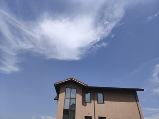 Poster - Single house under a blue sky with numerous fluffy clouds in the background