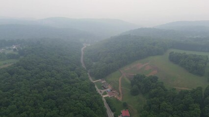 Wall Mural - Aerial footage of a roadside farm and dense woods on the green hills on a foggy morning