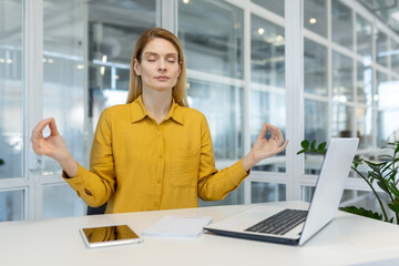 A businesswoman practices mindfulness meditation at her desk in a modern office, promoting workplace wellness and stress relief.