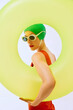 © master1305 - Elegant woman in green swim cap and white sunglasses, framed by large yellow inflatable ring, creating vibrant and eye-catching composition against white background. Concept of summer, retro fashion