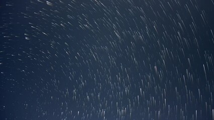 Wall Mural - nighttime time lapse of the stars moving through a dark blue sky. the stars are displayed as long co