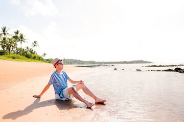 Wall Mural - A man sitting on the sandy beach, relaxing. enjoying summer vacation on a paradise beach