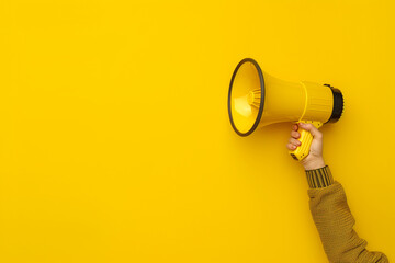 female hand holds a megaphone on a yellow background