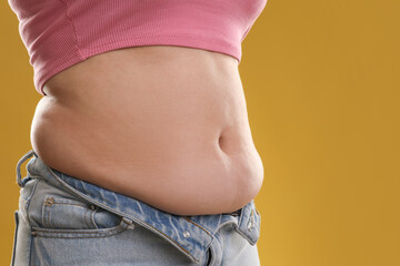 Wall Mural - Woman with excessive belly fat on goldenrod background, closeup. Overweight problem