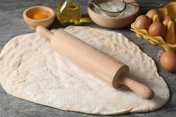 Raw dough, rolling pin and ingredients on grey table