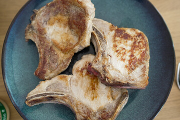 Top-down view of three cooked pork chops on a blue plate. The chops are beautifully seared, showing a balance of golden-brown crust and a hint of pink, promising a flavorful meal