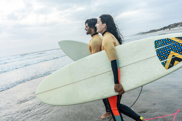 Wall Mural - Two friends sprint toward the water. Boards in hand, wetsuits on, they're poised for a ride through the waves, creating unforgettable memories together.	