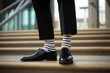 © ZMPixels - Legs with black pants, different pair of socks and black shoes standing on stairs outdoors. Young man foots in mismatched socks. Odd Socks day, Anti-Bullying Week, Down syndrome awareness concept