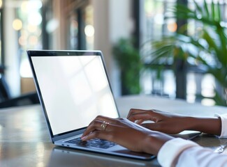 Wall Mural - Close up of a man's hands typing on a laptop with a blank white screen, the office background is blurred.