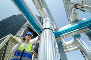 Industrial engineer adjusting pipeline valve with radio communication on construction site. Engineer on urban construction site using radio to coordinate with team on a sunny industrial rooftop.