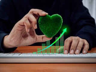 Wall Mural - Green business eco company and earth care sustainable development concepts. Rise arrow on digital growth graph with businessman hold green grass heart ball while working with computer in workplace.