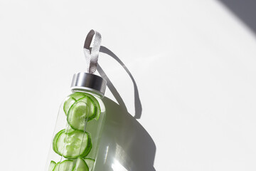 Wall Mural - Cleansing and refreshing cucumber water drink detox, shadow at sunlight on white with sun glare caustics. Wellness, alkaline diet, eating healthy concept. Stylish glass reusable water bottle