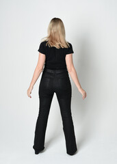 Canvas Print - Full length portrait of beautiful blonde woman wearing modern black shirt and leather pants. Confident  standing pose walking away from camera, silhouetted on white studio background.