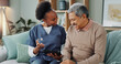 © peopleimages.com - Tablet, healthcare and nurse in home by senior man, internet and communication on wellness on sofa. African caregiver, elderly person and technology for learning or help and trust in chronic illness