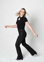 Canvas Print - Full length portrait of beautiful blonde woman wearing modern black shirt and leather pants. Confident standing pose with gestural hands presenting, silhouetted on white studio background.