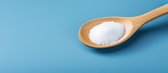 Poster - A wooden spoon contains white sugar with a blue background providing a copy space image