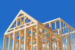 © ImageFlow - Wooden house frame under construction on a bright blue sky background, concept of home building. 3D Rendering.
