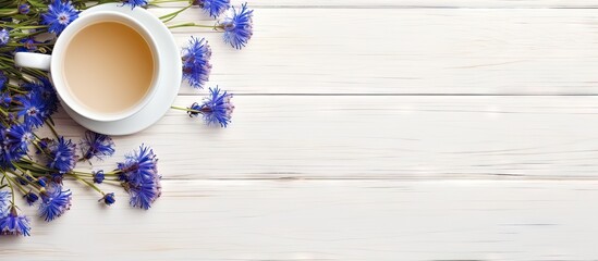 Wall Mural - Flat lay of a cup of tea and cornflowers on a white wooden table with ample copy space for adding text