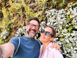 © simona - Happy couple middle age of tourist taking selfie picture together with leaves wall in background exploring city and destination. Traveler have fun in relationship. People and lifestyle with love