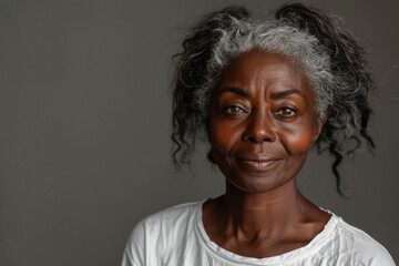 Wall Mural - Older black woman with grey hair in a white t-shirt against grey backdrop with copy space for ads