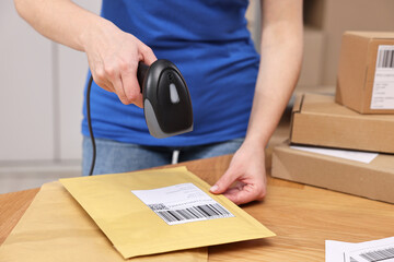 Sticker - Parcel packing. Post office worker with scanner reading barcode at wooden table indoors, closeup