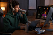© New Africa - Young man with energy drink and headphones playing video game at wooden desk indoors