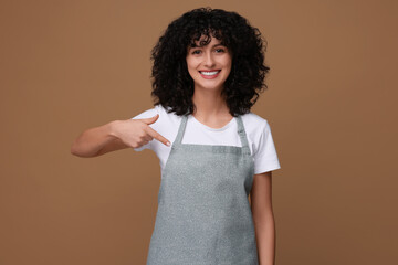 Wall Mural - Happy woman pointing at kitchen apron on brown background. Mockup for design