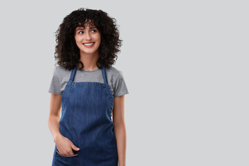 Wall Mural - Happy woman wearing kitchen apron on light grey background, space for text. Mockup for design