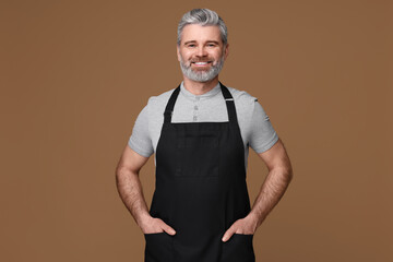 Wall Mural - Happy man wearing kitchen apron on brown background. Mockup for design