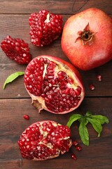 Fresh pomegranates and green leaves on wooden table, flat lay