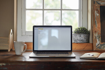 Table, notebook and screen of laptop in house for email, digital connection and networking. Interior, window and mockup with technology on desk for application, communication and search on website