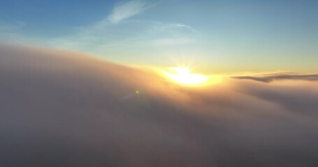 Wall Mural - Aerial footage over the clouds of glowing sun with rays and blue sky at sunset