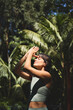 © insta_photos - Calm young Hispanic woman holding hands in namaste meditating doing yoga breathing exercises with eyes closed feeling peace of mind, mental balance standing in green nature tropical park. Vertical.