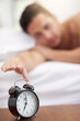 © peopleimages.com - Morning, bed and hand of person for alarm to snooze, switch off and wake up in home. House, bedroom and ring of clock for sleeping or dreaming, resting and exhausted man in apartment as routine