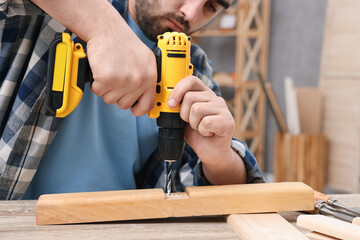 Canvas Print - Young handyman working with electric drill at table in workshop, closeup