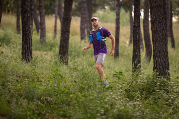 A man is running through a forest wearing a purple shirt and blue backpack