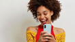 © jodoto - Excited Woman Using Smartphone - Joyful woman with curly hair looking at her smartphone, celebrating a happy moment, dressed in a bright yellow top.