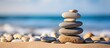 © StockKing - A zen symbol in the form of a pyramid of stones resting on sandy ground representing harmony and balance The image also includes the serene backdrop of the ocean with a closeup of a tower of sea pebb