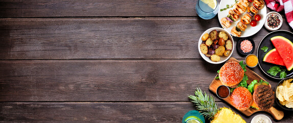 Wall Mural - Summer BBQ food side border. Hamburgers, meat skewers, potatoes, fruit and snacks. Top down view on a dark wood banner background. Copy space.