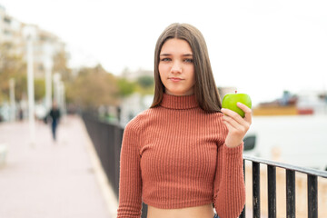 Poster - Teenager girl with an apple at outdoors with sad expression