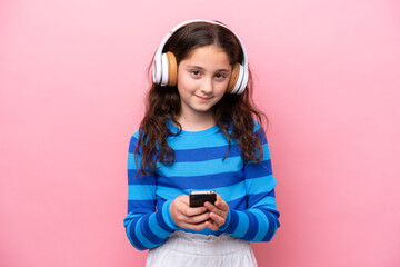 Wall Mural - Little girl isolated on pink background listening music with a mobile and looking front