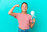 Fototapeta Na drzwi - Little Caucasian girl holding a lollipop isolated on blue background doing strong gesture