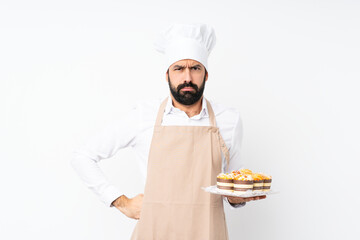 Wall Mural - Young man holding muffin cake over isolated white background angry
